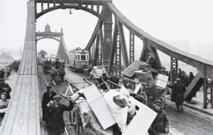czarno biała fotografia przedstawiająca ludność cywilną przenosząca i przewożącą swój dobytek poprzez Most Podgórski 