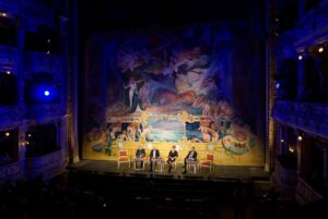 Sesja inauguracyjna, panel dyskusyjny „Prawo dla dziedzictwa” w Teatrze im. Juliusza Słowackiego w ramach III Kongresu Konserwatorów Polskich. Na scenie, przed bogato zdobioną kurtyną z barwnym malowidłem przedstawiającym postacie mitologiczne, siedzi czworo panelistów przy stolikach. Wnętrze teatru o złotych dekoracjach i balkonach jest oświetlone niebieskim światłem.